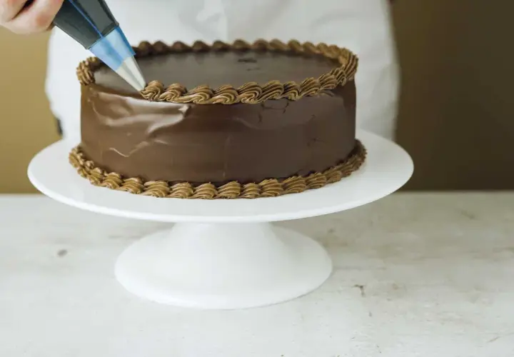En chokladtårta dekoreras med en sprits med chokladfrosting. Ett perfekt resultat med detta ganache recept.