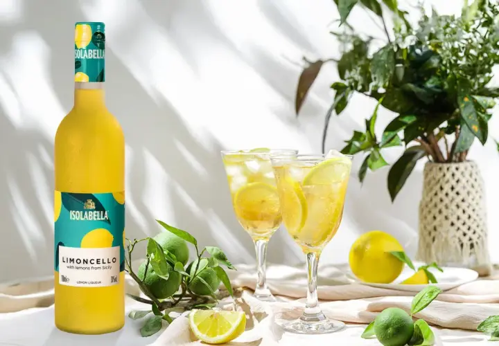 En flaska Isolabella Limoncello står bredvid två glas med is och citron. Perfekt för ett somrigt limoncello recept.