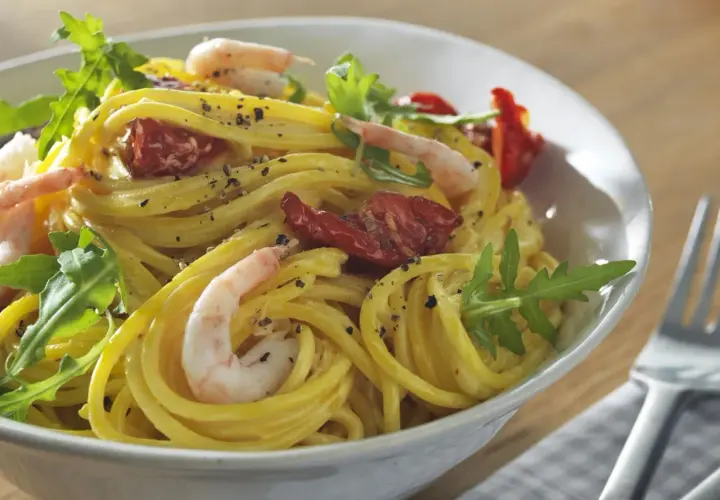 En skål med gyllene zafferano pasta med räkor, soltorkade tomater och ruccola. En härlig måltid!