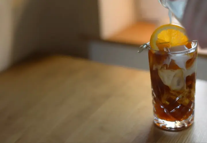 En hand häller mjölk i ett glas med iskaffe, garnerat med en apelsinskiva. Ett perfekt iskaffe recept för en varm dag.