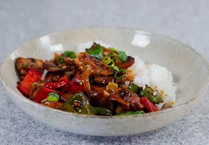 En skål med ris och en smakrik kyckling cashew-röra med paprika och svamp, toppad med salladslök.
