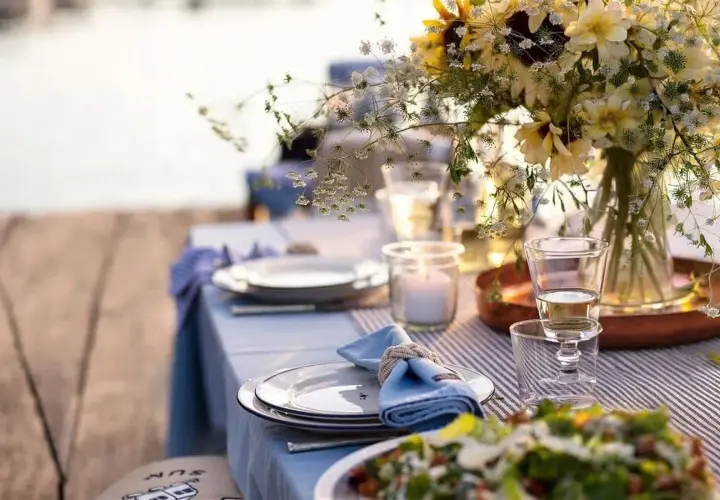 Vacker dukning vid vattnet för ett somrigt mat midsommar. Blommor, ljus och tallrikar redo för fest.