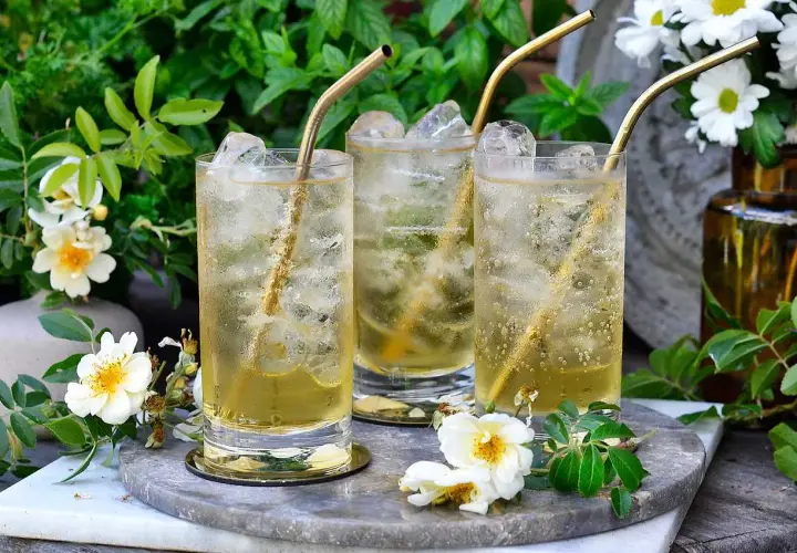 Tre glas med is och gyllene sugrör. En uppfriskande geting drink i en lummig trädgård.