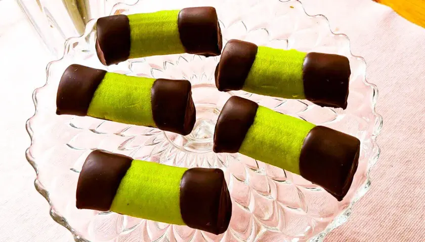Fem gröna dammsugare bakverk med chokladtoppar ligger på ett glasfat.