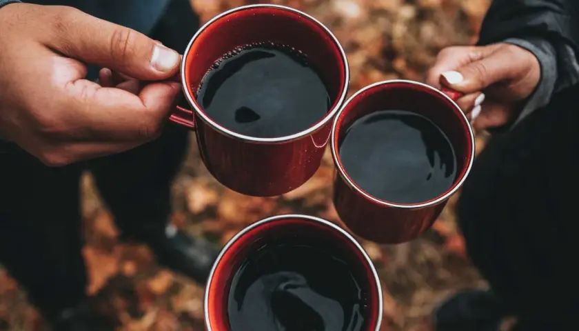 Händer håller röda muggar med varmt kaffe. En mysig stund utomhus, perfekt för att koka kaffe.