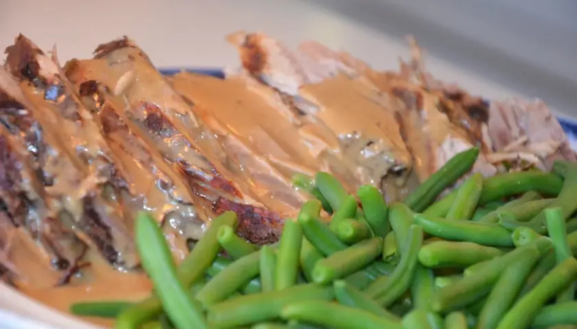 Skinkstek i gryta, saftig och uppskuren, serveras med en krämig sås och gröna bönor. En klassisk och smakrik rätt.