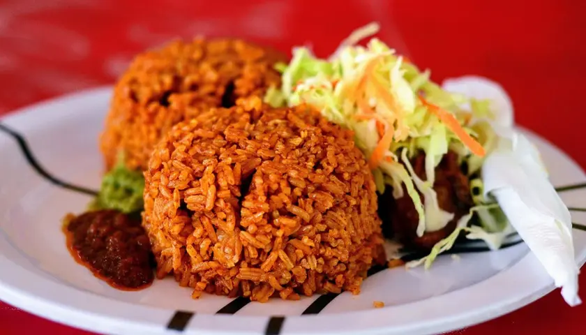 Två portioner jollof rice med sallad och en kryddig sås. En smakrik rätt som lockar.