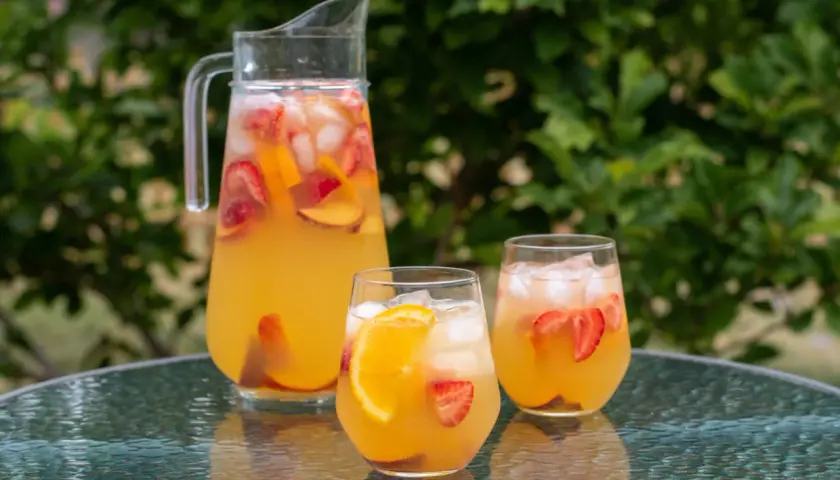 En karaff och två glas med uppfriskande cava sangria fylld med frukt och is, redo att avnjutas utomhus.