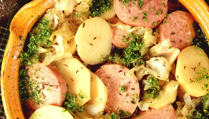 En värmande korvgryta med potatis, kål och persilja i en rustik keramikskål.