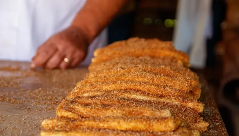 En hand lägger socker och kanel på en stapel nygjorda churros. Dessa friterade godsaker är ett populärt sätt att svara på frågan "vad är churros".