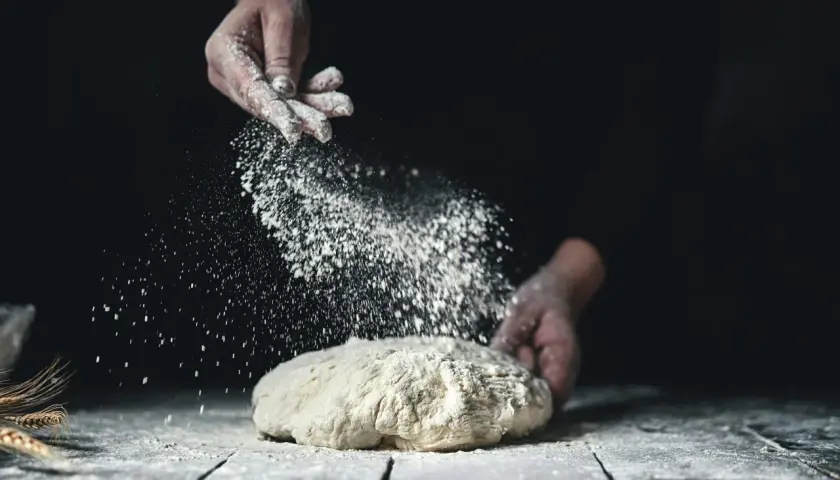 Händer strör mjöl över deg. Vete och råg ger en härlig doft av nybakat bröd.