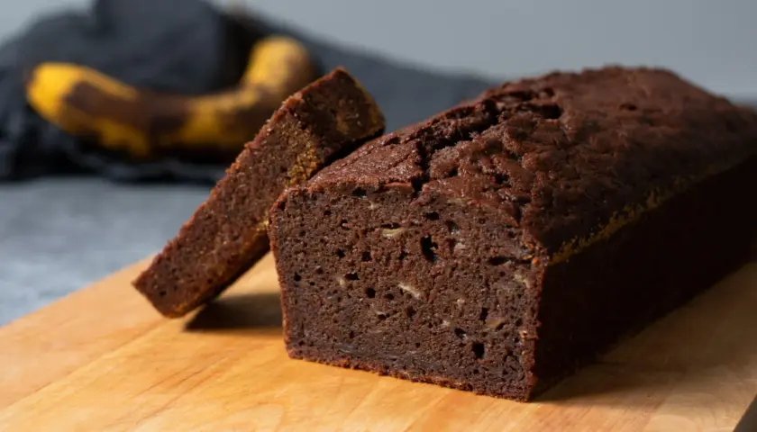 En saftig banan sockerkaka med en skiva uppskuren, redo att avnjutas. En övermogen banan ligger i bakgrunden.