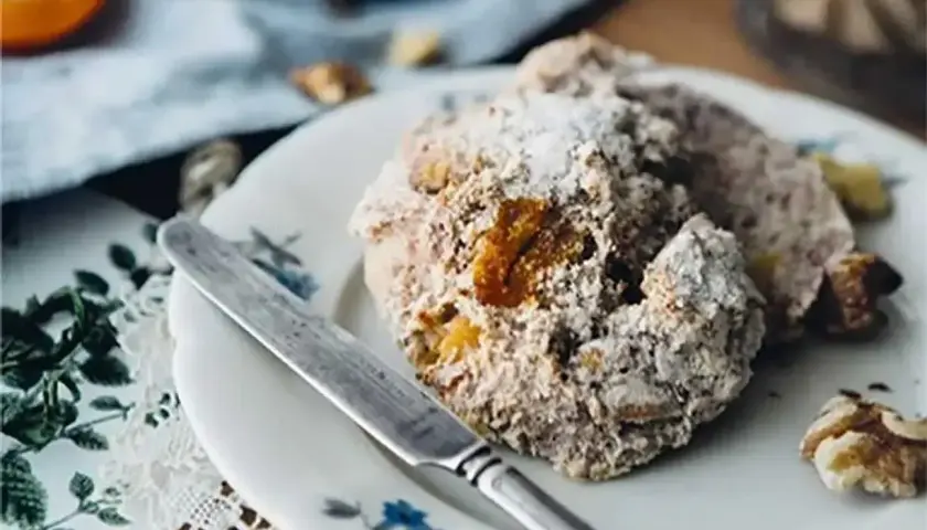 En tallrik med hembakat vetedeg recept, pudrat med florsocker och nötter. En kniv ligger bredvid.