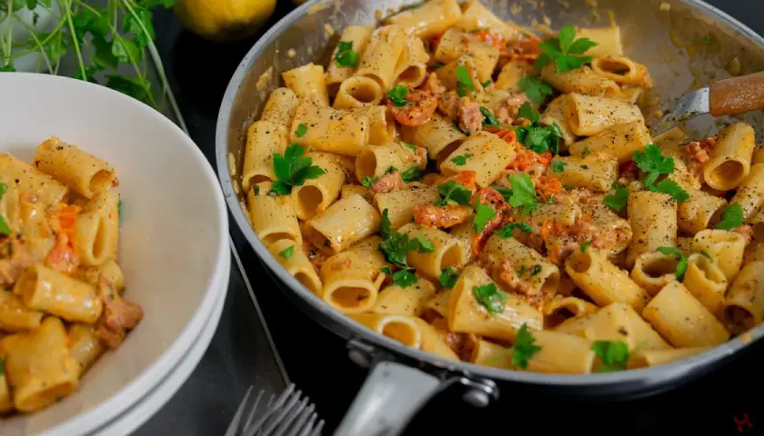 En krämig salsiccia pasta med rigatoni, toppad med färsk persilja och nymalen svartpeppar. En portion serveras i en vit skål.