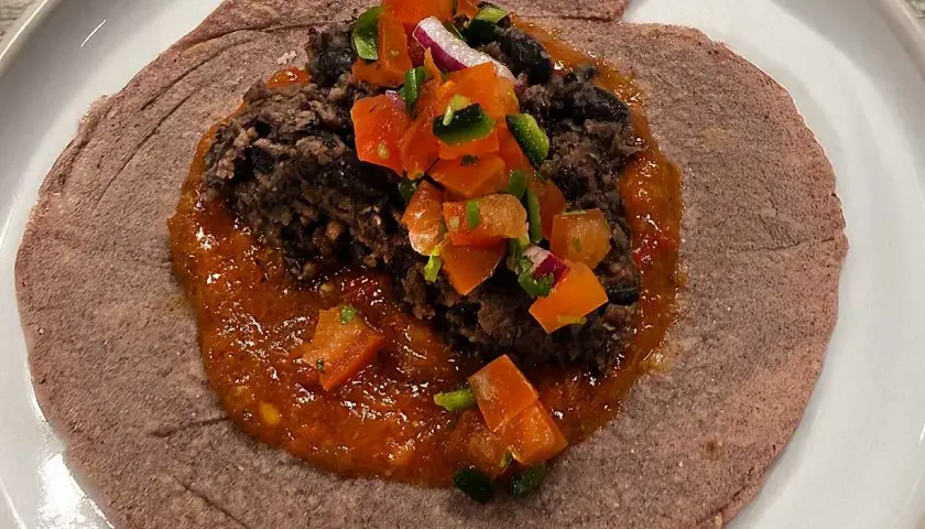 En lila tortilla med en klick refried beans, salsa och hackade grönsaker.