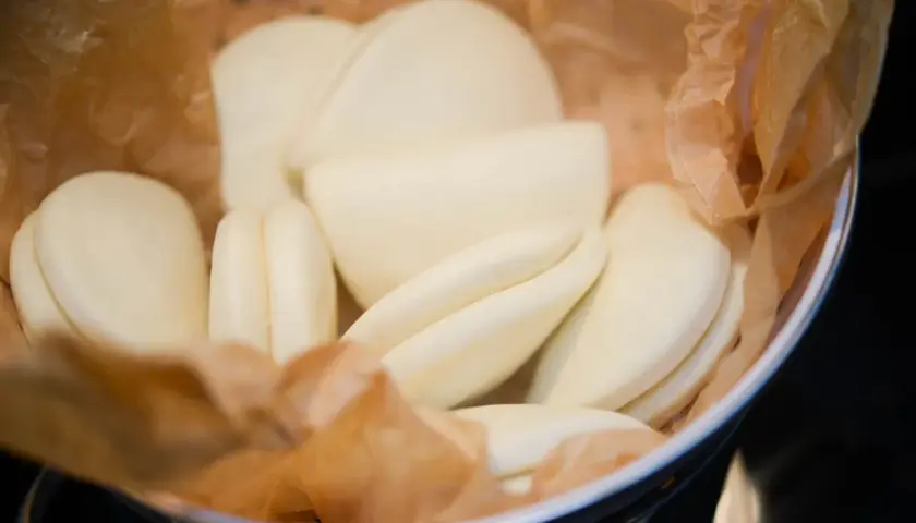 En skål med ångade bao buns, inlindade i bakplåtspapper. De är mjuka, vita och redo att fyllas med goda saker.