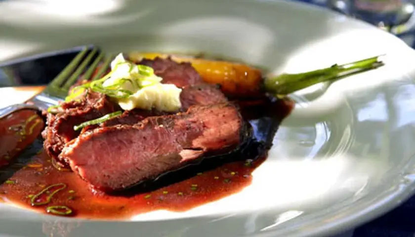 Skivat flat iron steak med en klick vitlöksdressing och en grön sparris.