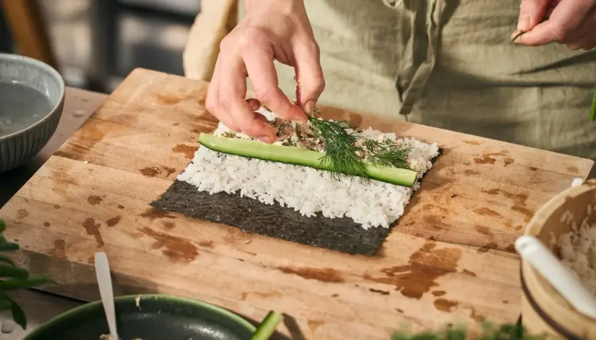 Händer lägger dill på ris och gurka för ett sushi recept.