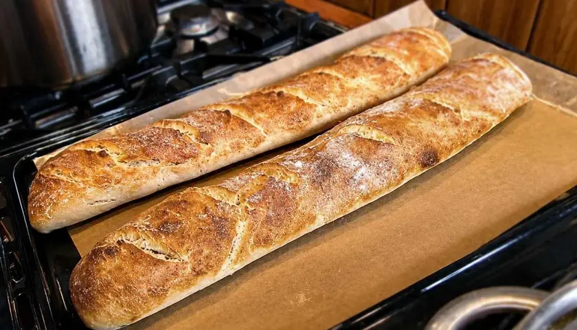 Två gyllenbruna surdegsbaguetter på bakplåtspapper, redo att avnjutas. Ett perfekt surdegsbaguette recept!
