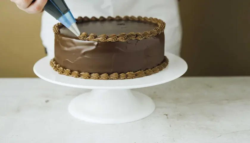 En chokladtårta dekoreras med en sprits med chokladfrosting. Ett perfekt resultat med detta ganache recept.