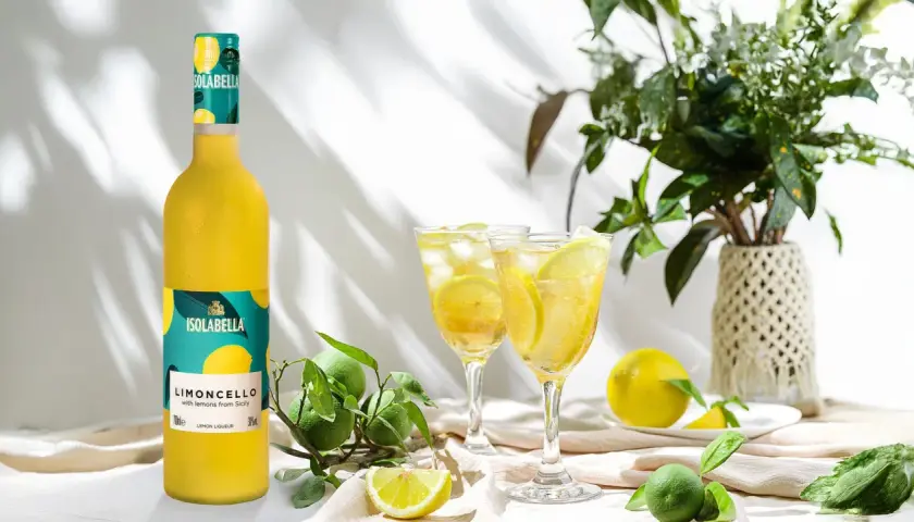 En flaska Isolabella Limoncello står bredvid två glas med is och citron. Perfekt för ett somrigt limoncello recept.