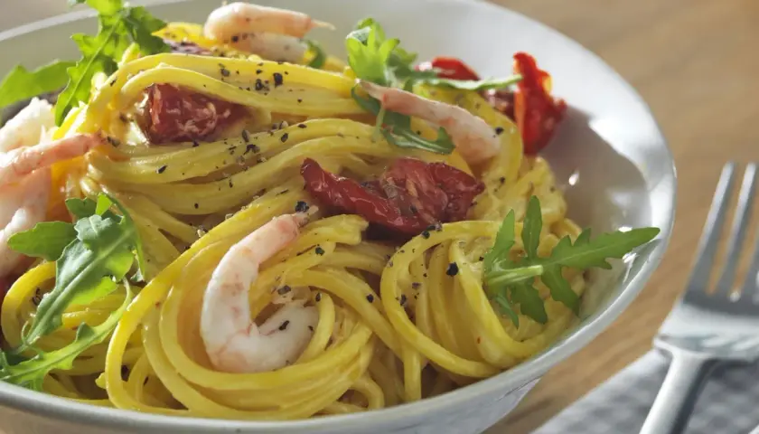 En skål med gyllene zafferano pasta med räkor, soltorkade tomater och ruccola. En härlig måltid!