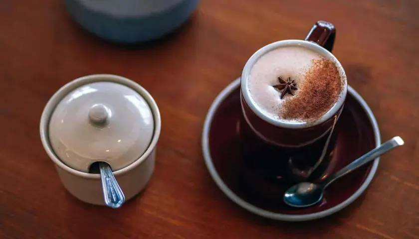 En kopp värmande chai latte med stjärnanis och kanel, perfekt för ett mysigt chai latte recept. Bredvid står en sockerskål med sked.