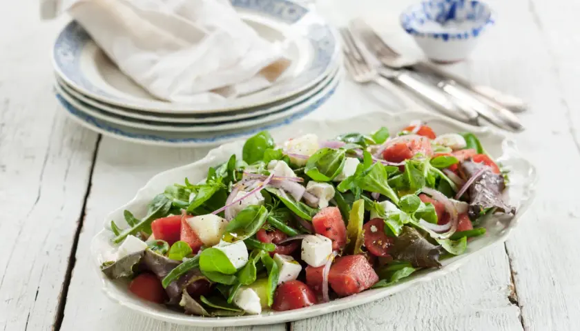 En uppfriskande melonsallad med fetaost, färska gröna blad, tomater och rödlök, ringlad med olivolja. Perfekt sommarbuffé!