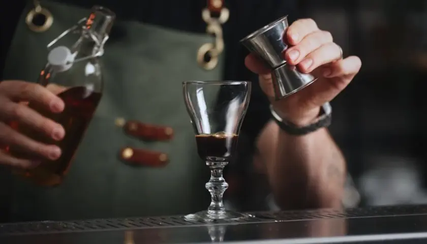 En bartender häller upp en mörk vätska i ett glas, kanske för att skapa en Leonard Sachs drink.