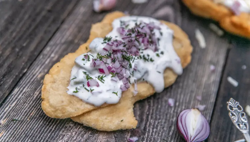En friterad langos med gräddfil, hackad rödlök och dill. Perfekt för ett snabbt langos recept.