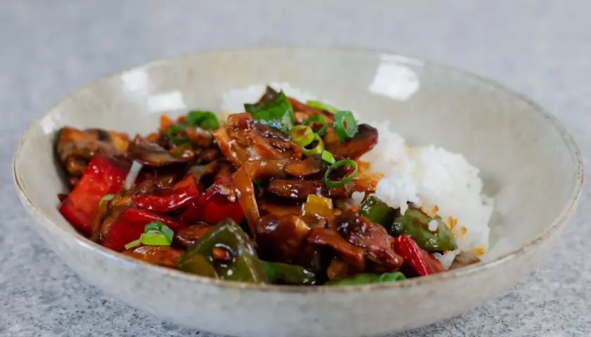 En skål med ris och en smakrik kyckling cashew-röra med paprika och svamp, toppad med salladslök.