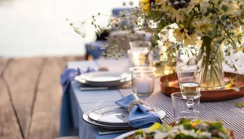 Vacker dukning vid vattnet för ett somrigt mat midsommar. Blommor, ljus och tallrikar redo för fest.