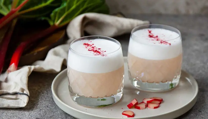Två glas med en krämig rabarber sour, toppad med skum och strödd med rabarberpulver. En härlig sommardrink!