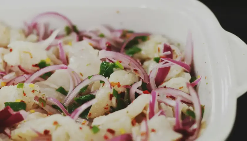 En närbild på en skål med färsk ceviche, med bitar av vit fisk, rödlök, chili och örter. Perfekt för ett somrigt ceviche recept.