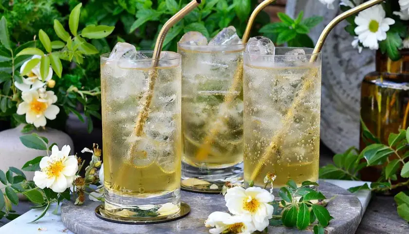 Tre glas med is och gyllene sugrör. En uppfriskande geting drink i en lummig trädgård.