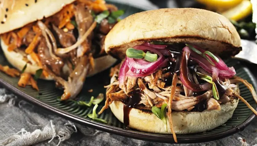 Två saftiga pulled pork burgare med rödlök och groddar på en mörk tallrik.