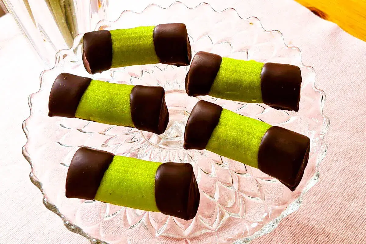 Fem gröna dammsugare bakverk med chokladtoppar ligger på ett glasfat.