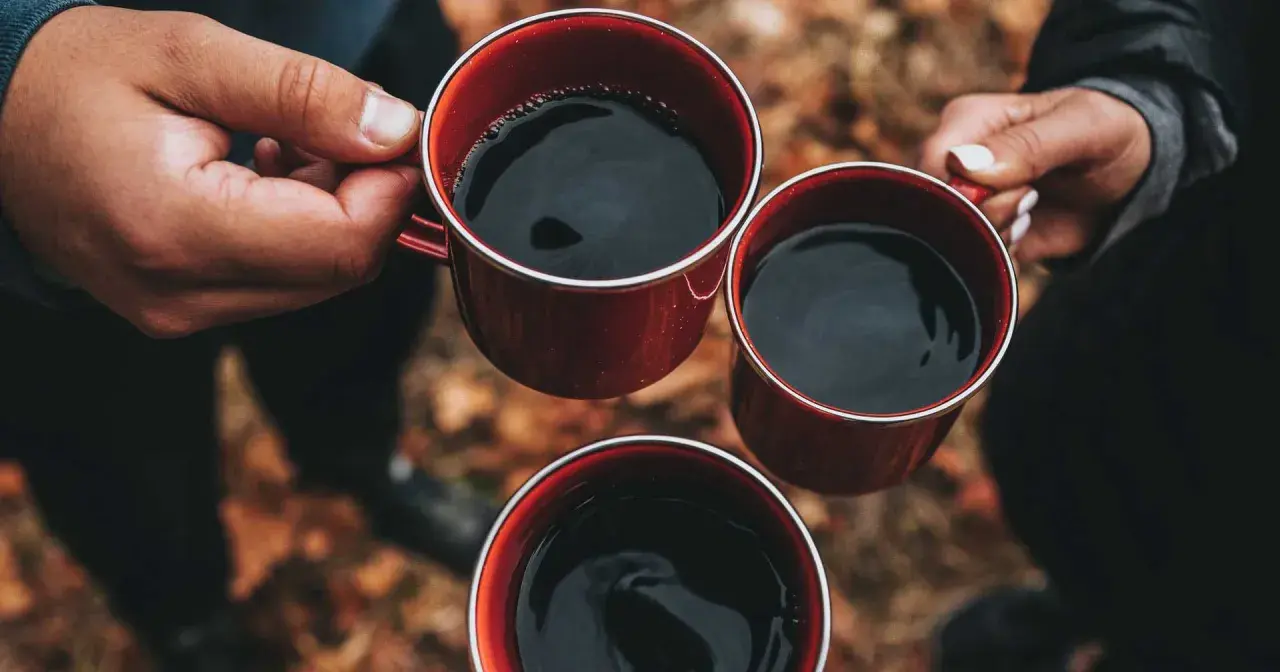 Händer håller röda muggar med varmt kaffe. En mysig stund utomhus, perfekt för att koka kaffe.