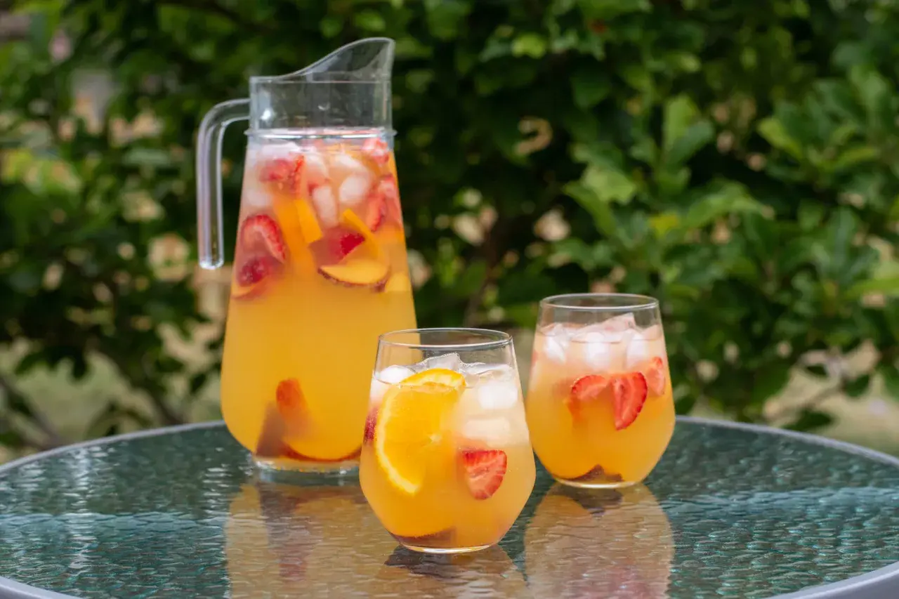 En karaff och två glas med uppfriskande cava sangria fylld med frukt och is, redo att avnjutas utomhus.