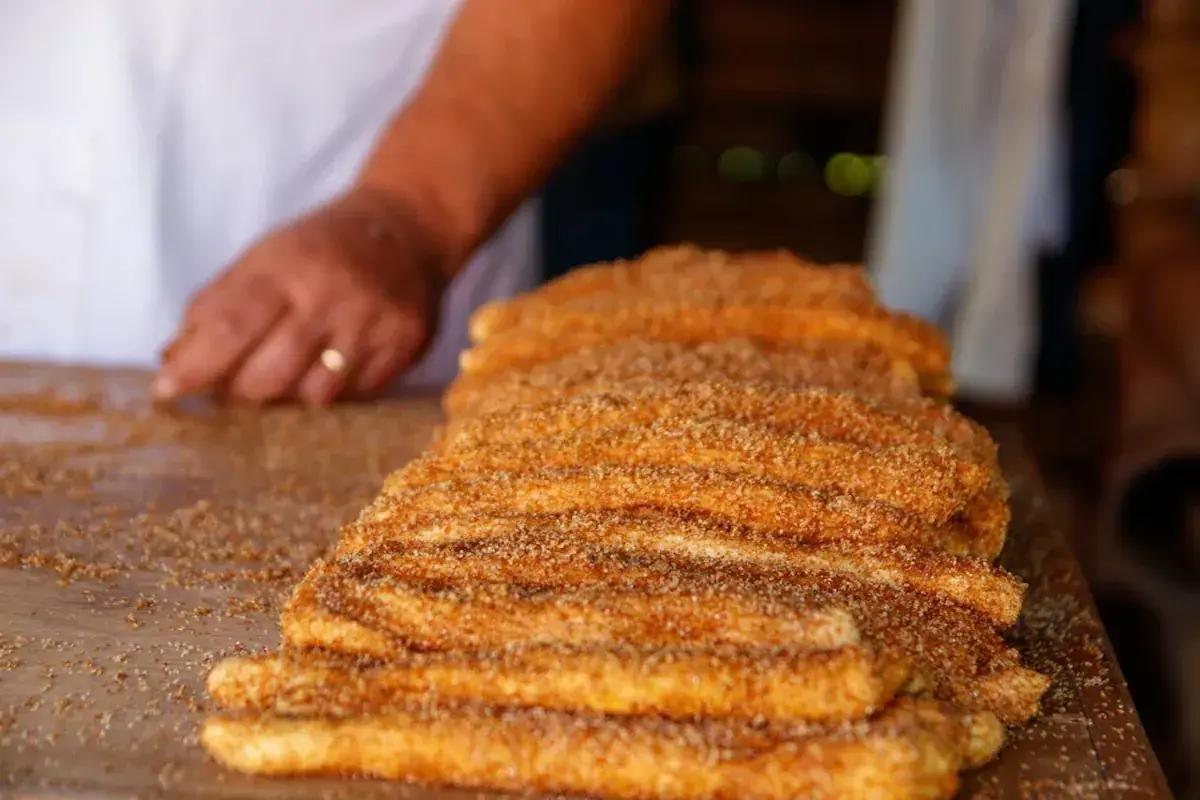 En hand lägger socker och kanel på en stapel nygjorda churros. Dessa friterade godsaker är ett populärt sätt att svara på frågan "vad är churros".