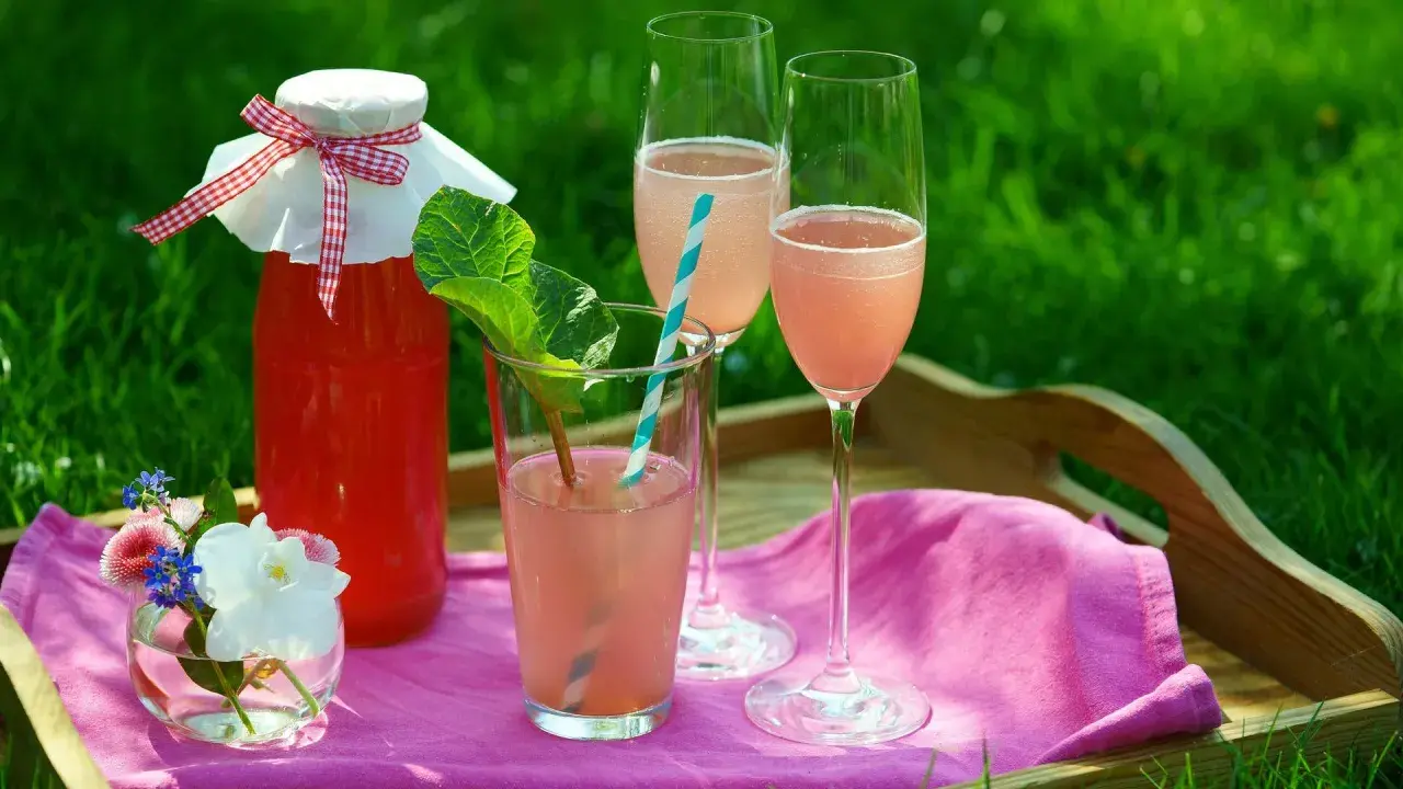 En flaska rabarberdrink och två glas prosecco på en bricka i gräset. En härlig sommardrink!