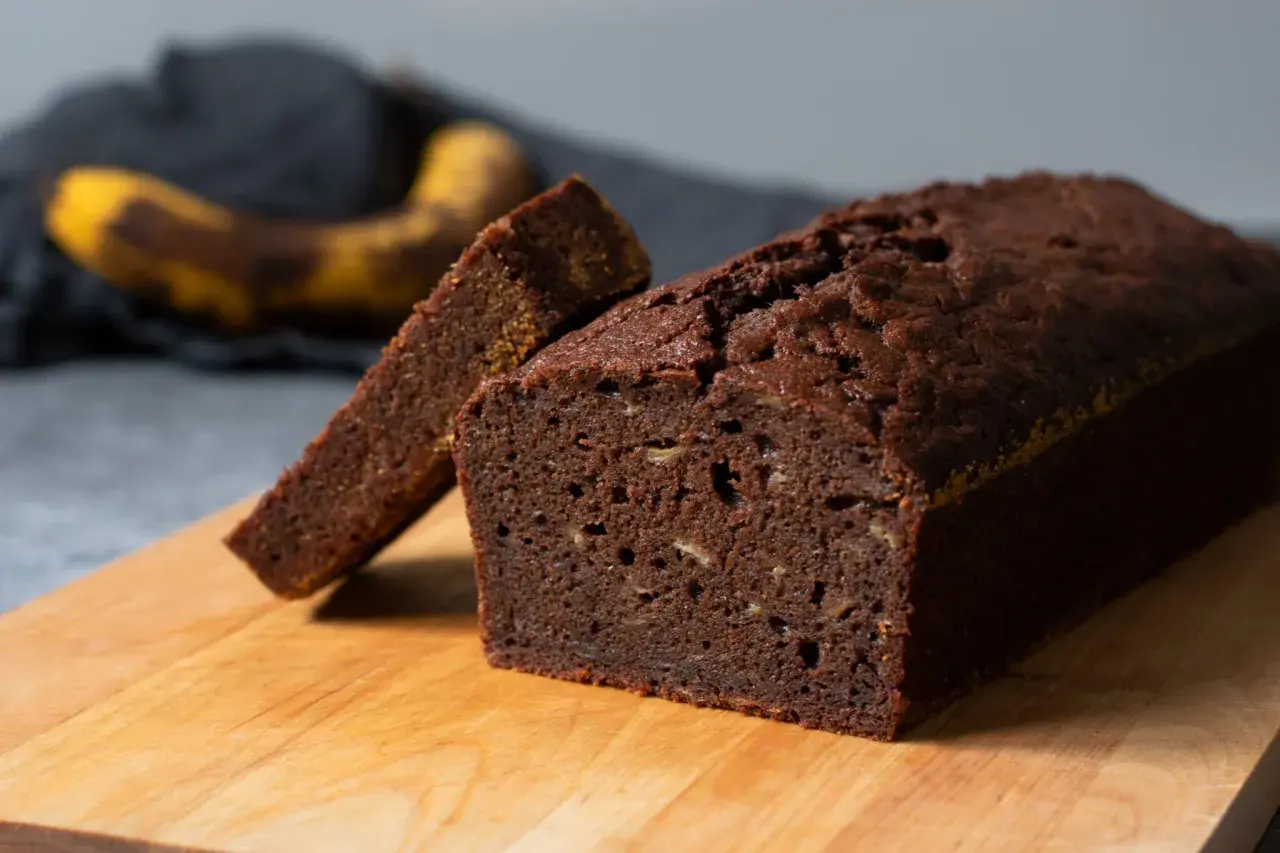 En saftig banan sockerkaka med en skiva uppskuren, redo att avnjutas. En övermogen banan ligger i bakgrunden.