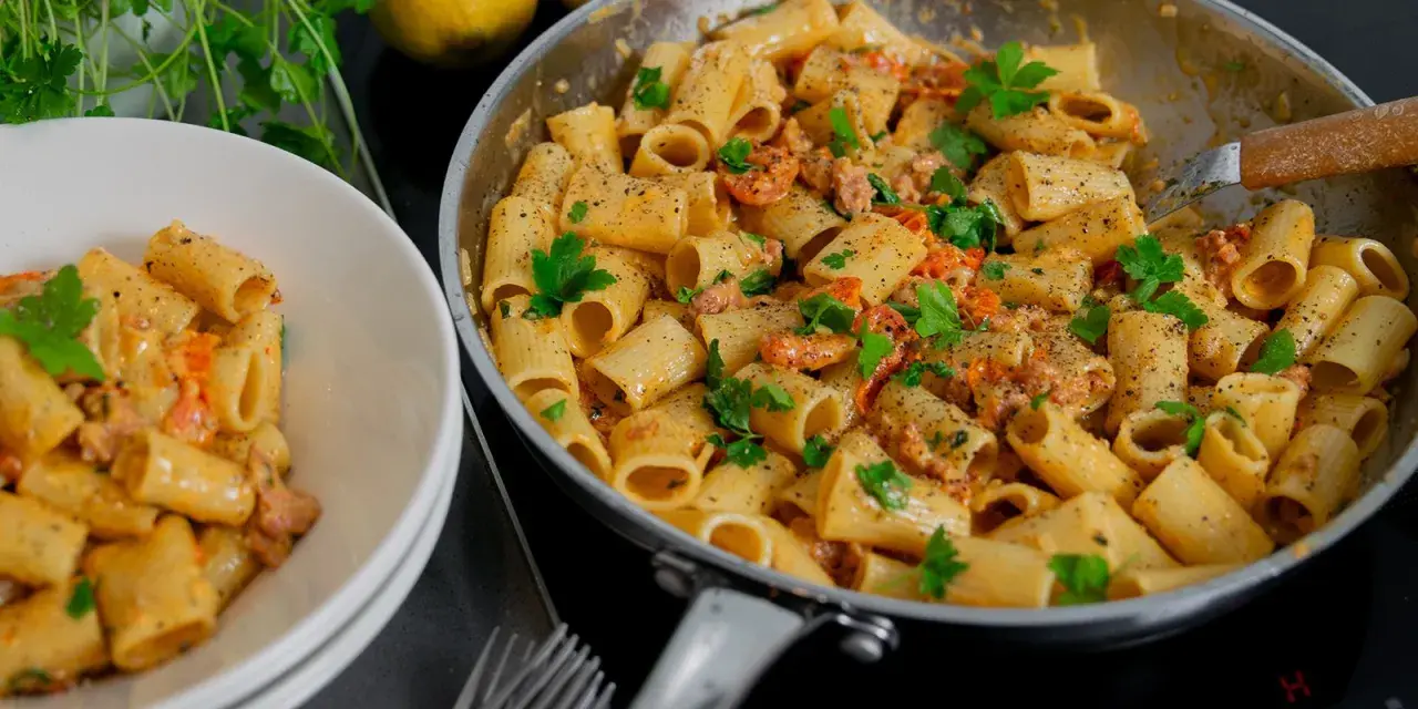 En krämig salsiccia pasta med rigatoni, toppad med färsk persilja och nymalen svartpeppar. En portion serveras i en vit skål.