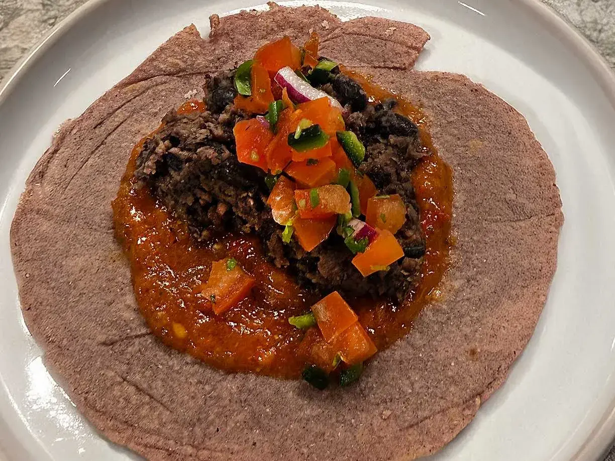 En lila tortilla med en klick refried beans, salsa och hackade grönsaker.