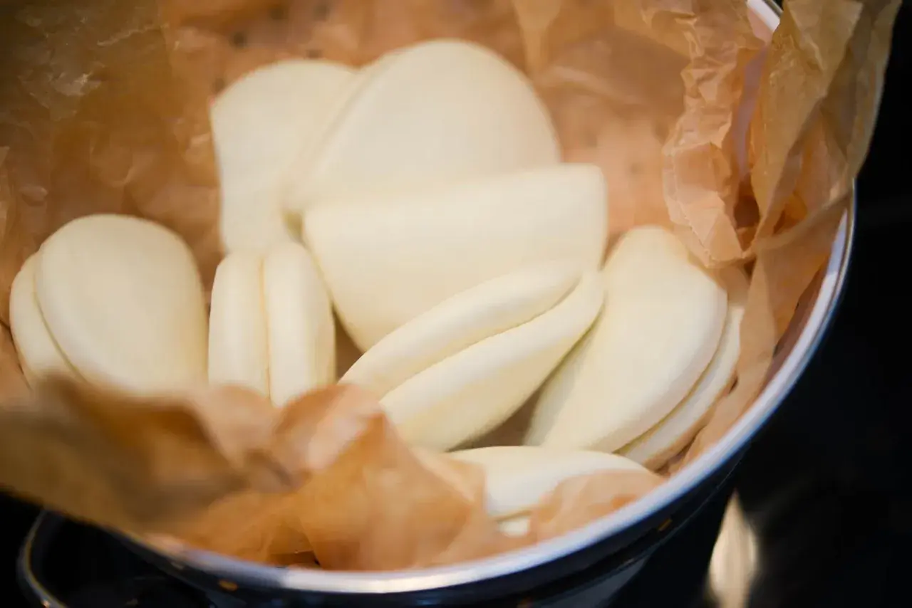 En skål med ångade bao buns, inlindade i bakplåtspapper. De är mjuka, vita och redo att fyllas med goda saker.