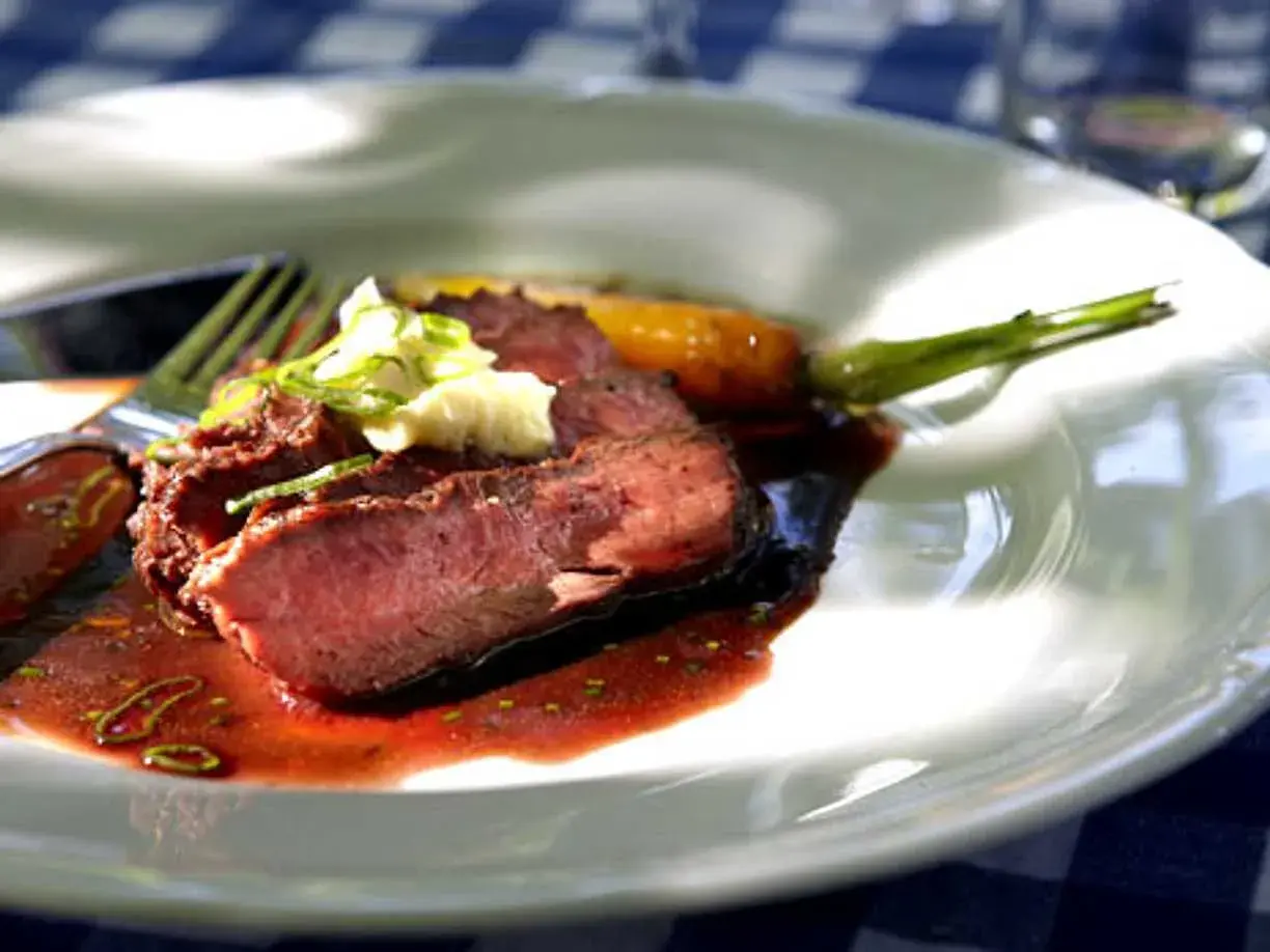 Skivat flat iron steak med en klick vitlöksdressing och en grön sparris.