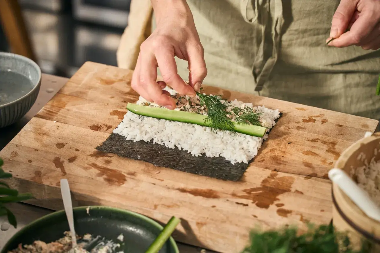 Händer lägger dill på ris och gurka för ett sushi recept.