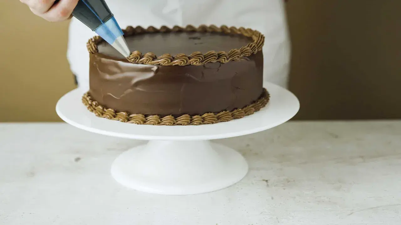 En chokladtårta dekoreras med en sprits med chokladfrosting. Ett perfekt resultat med detta ganache recept.