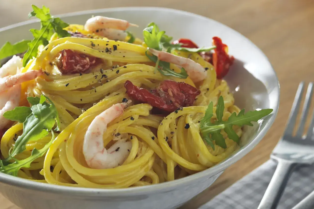 En skål med gyllene zafferano pasta med räkor, soltorkade tomater och ruccola. En härlig måltid!