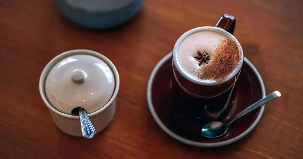 En kopp värmande chai latte med stjärnanis och kanel, perfekt för ett mysigt chai latte recept. Bredvid står en sockerskål med sked.